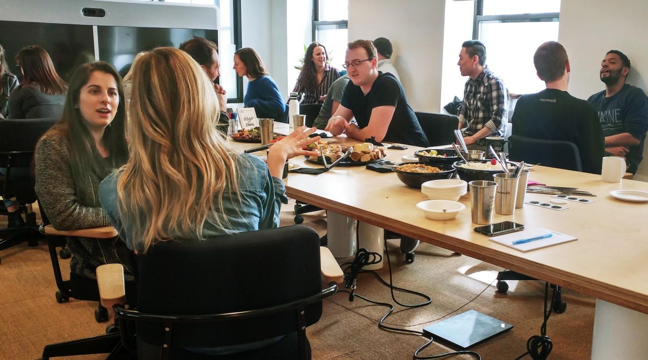 MPFG participants collaborating around table with laptops and materials in bright modern workspace